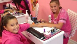 Young girl in pink robe getting a manicure from a brunette woman in a pink uniform